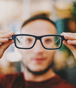 A man holds glasses out in front of his face. We offer eye care for adults and children as well as emergency eye care.